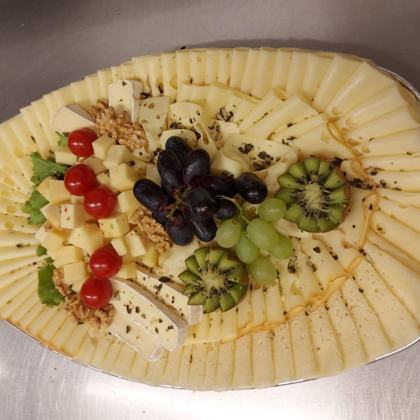 Eine Käseplatte mit verschiedenen Käsesorten, Trauben, Kiwis und roten Kirschen, garniert mit Nüssen und Kräutern auf einer Metalloberfläche.
