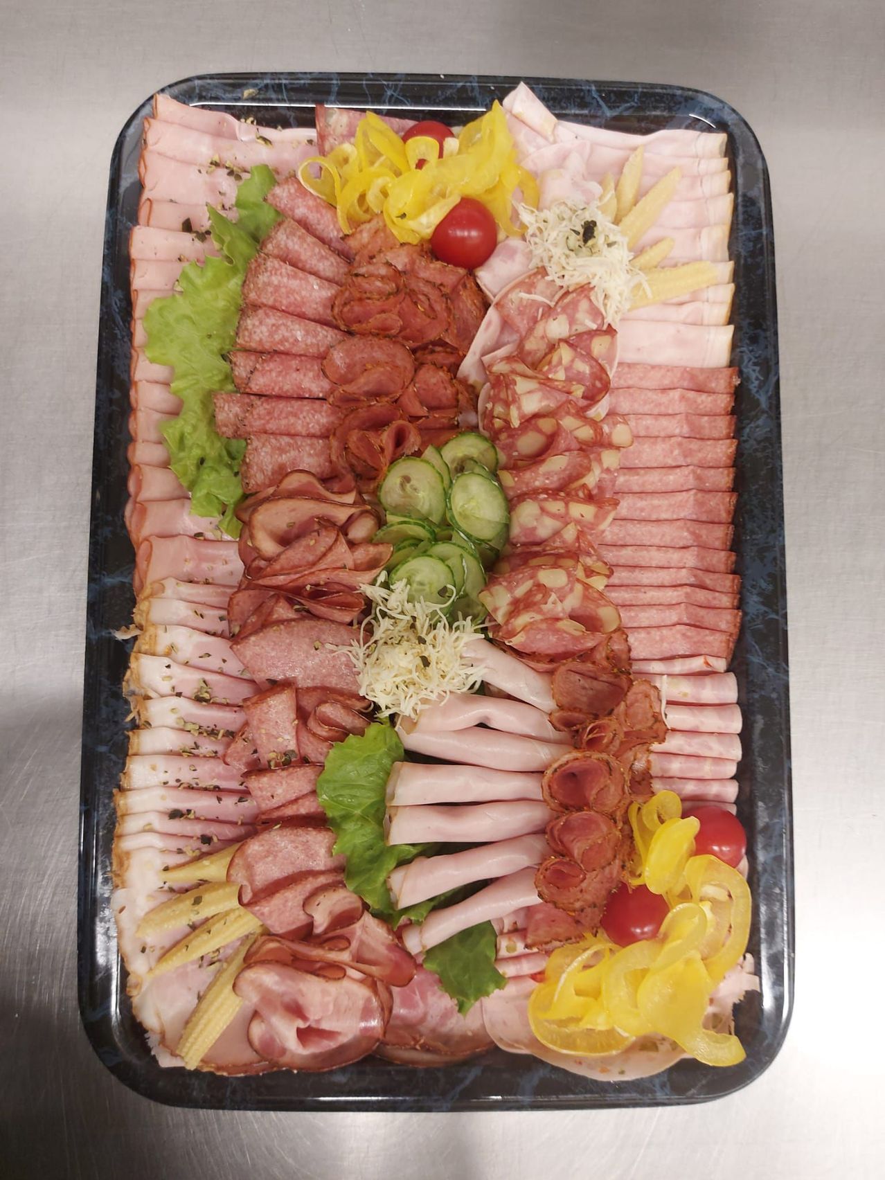 Ein Fleischplatten mit verschiedenen Scheiben von Wurst, Gurken, Tomaten und Käse. Die Platte wird auf einem schwarzen Tablett mit einer marmorierten Oberfläche serviert.