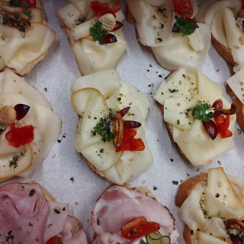 Eine Auswahl an Vorspeisen mit Käse- und Schinkenscheiben, garniert mit Kräutern, Tomaten und Pilzen auf weißem Pergamentpapier.