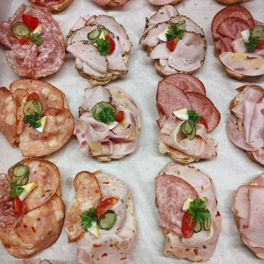 Eine Nahaufnahme verschiedener Aufschnitte auf Brotscheiben, garniert mit Gurken, Tomaten und Kräutern.