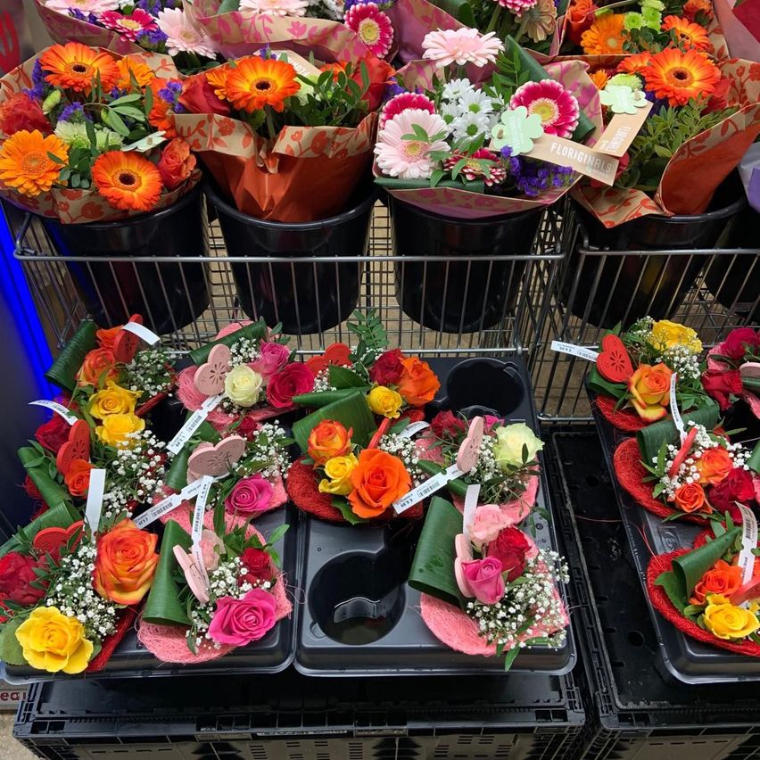 A display of assorted flowers in various colors and sizes. Some flowers are in buckets, while others are in decorative holders on trays. The flowers are arranged in a way that resembles a flower shop.