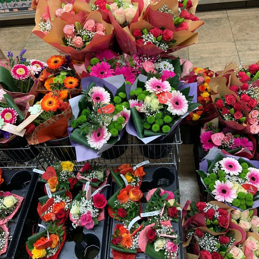 A collection of assorted flower bouquets are displayed in a store. Each bouquet is wrapped in different colored paper, some with tags. The flowers include roses, daisies, and carnations.