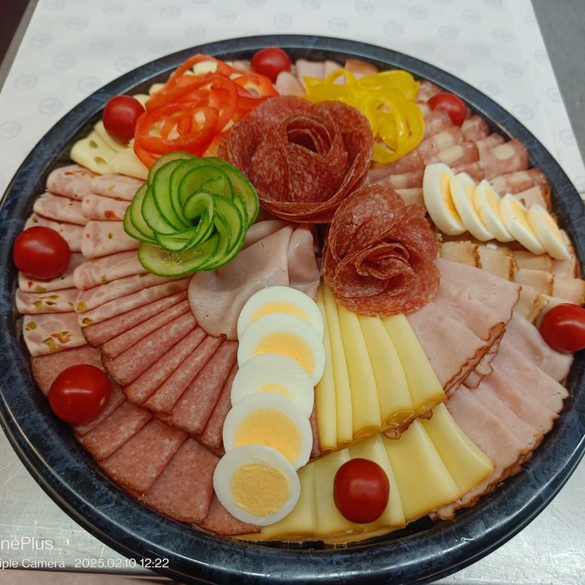 Eine Platte mit verschiedenen Fleischsorten, Käse und Gemüse, darunter geschnittener Schinken, Salami, gekochte Eier und Gurkenblüten.