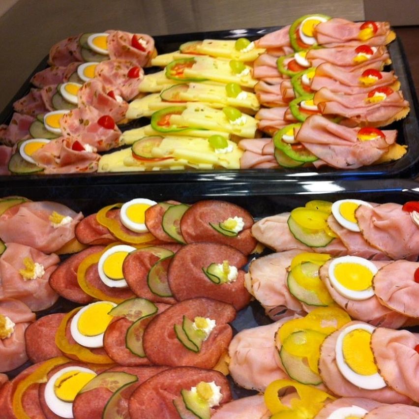 Zwei Tabletts mit Sandwiches aus Schinken, Käse, Eiern und Gurken. Die Sandwiches sind so angeordnet, dass sie ein kreisförmiges Muster bilden.