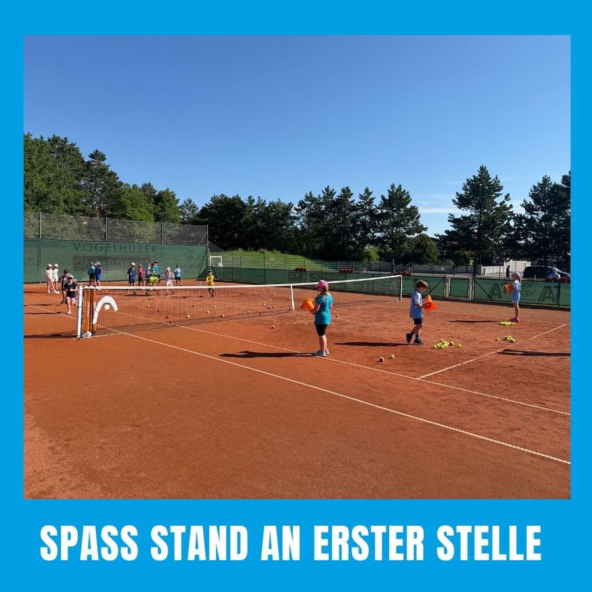 Ein Tennisplatz mit spielenden Menschen und Kindern, einem Netz in der Mitte und einem Schild, das 'Spass Stand an erster Stelle' besagt.