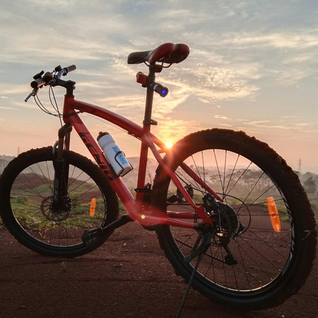 Ein rotes Mountainbike mit einer Wasserflasche ist auf einem Feldweg bei Sonnenuntergang geparkt.