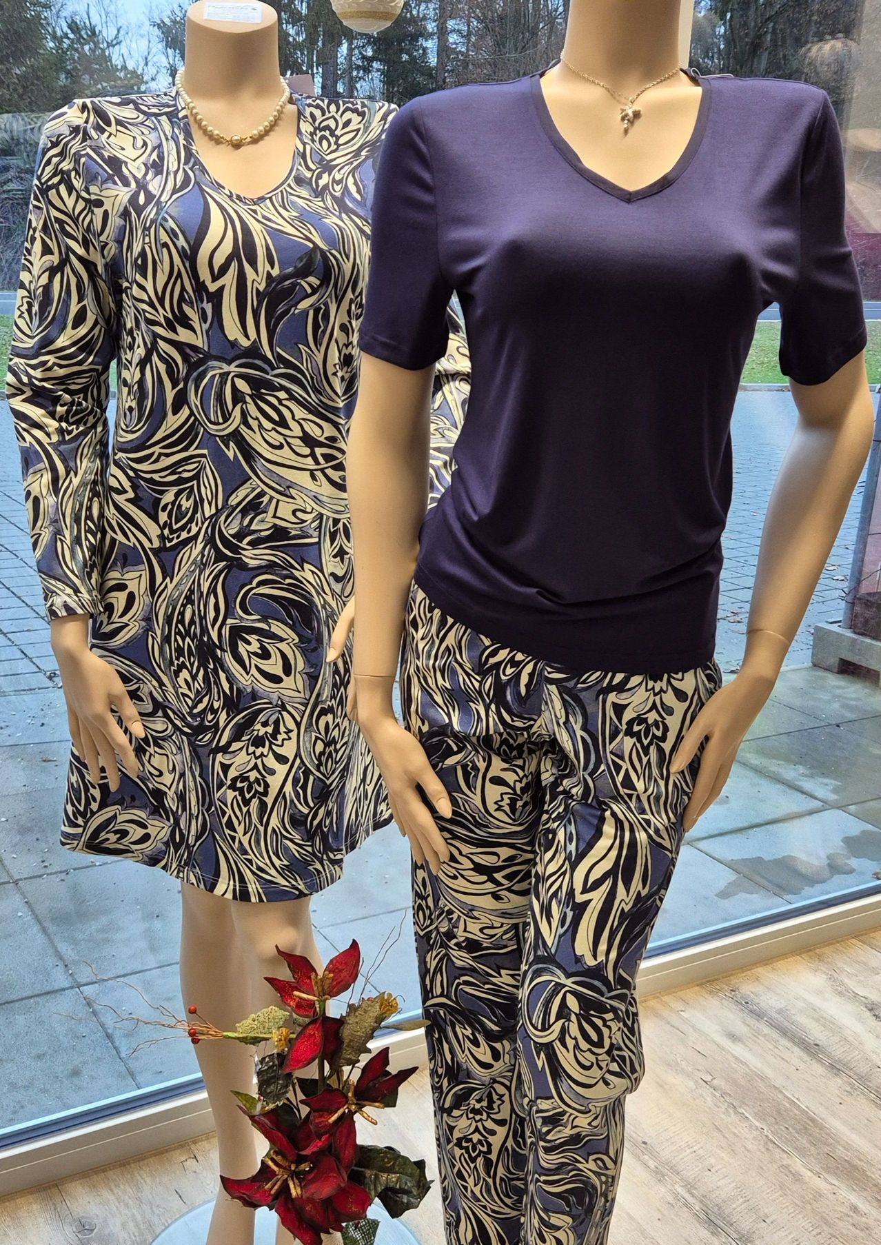 Zwei Mannequins in einem Schaufenster präsentieren ein blaues Blumenkleid und ein marineblaues V-Ausschnitt-Shirt und eine Hose mit ähnlichem Muster.