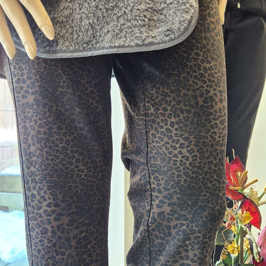 Eine Puppe trägt eine schwarze Hose mit Leopardenmuster und hält ein graues Tuch in den Händen.