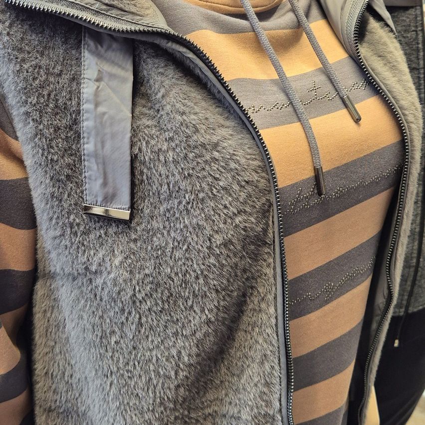 Eine Nahaufnahme einer grauen Pelzjacke mit Reißverschluss und gestreiftem Innenhemd zeigt Details der Stofftextur.