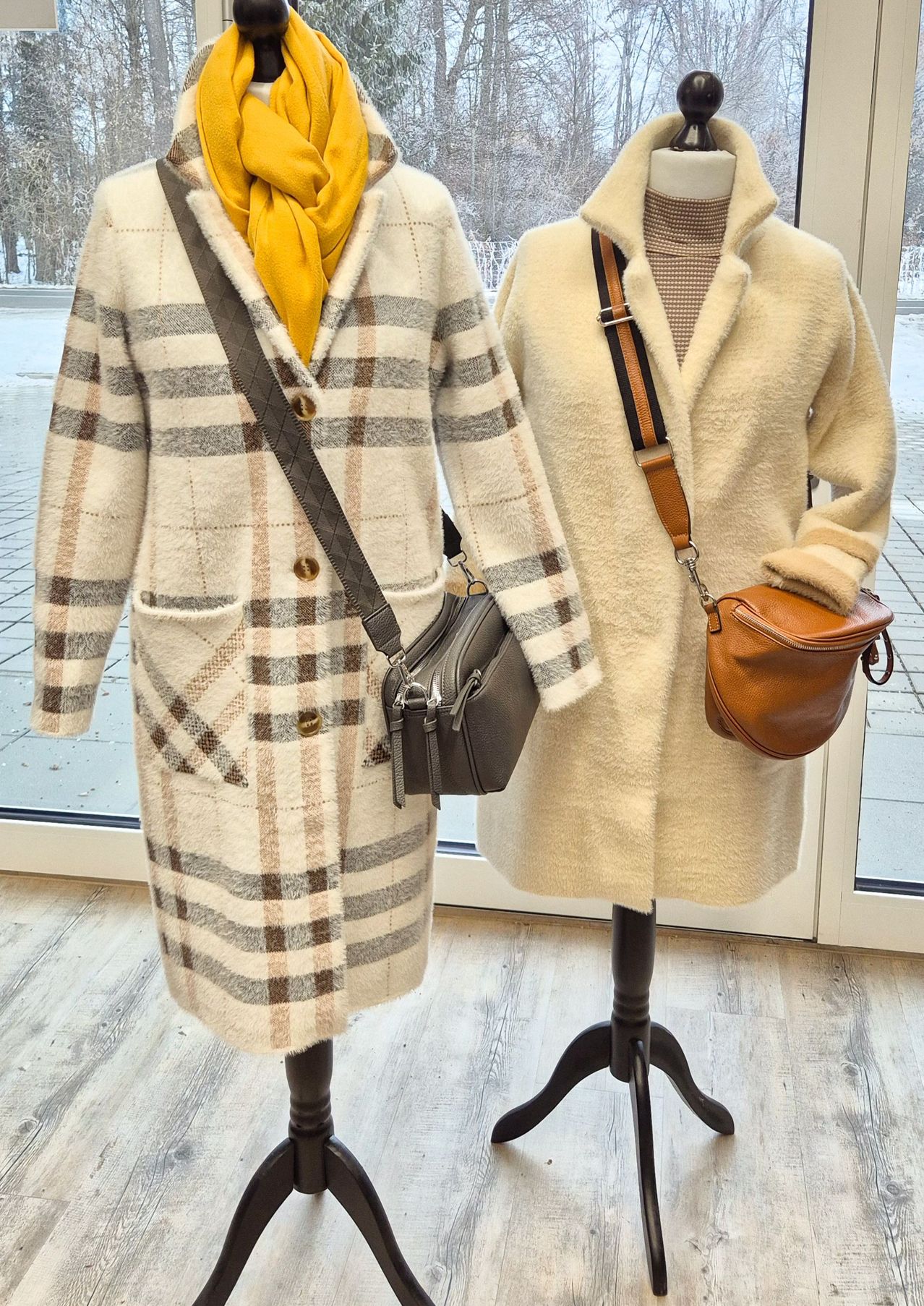 Two winter coats on mannequins, one is plaid and the other is cream-colored, both with bags on their shoulders.