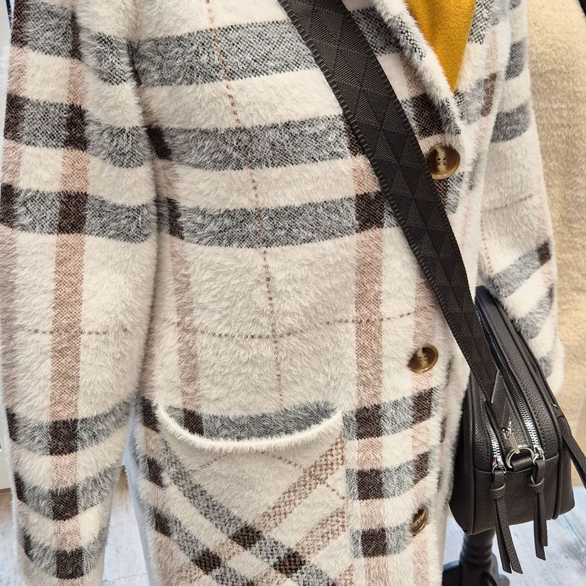 A close-up of a plaid fur-lined coat with buttons and a black strap. The coat is white, gray, and brown. A black handbag is beside it.