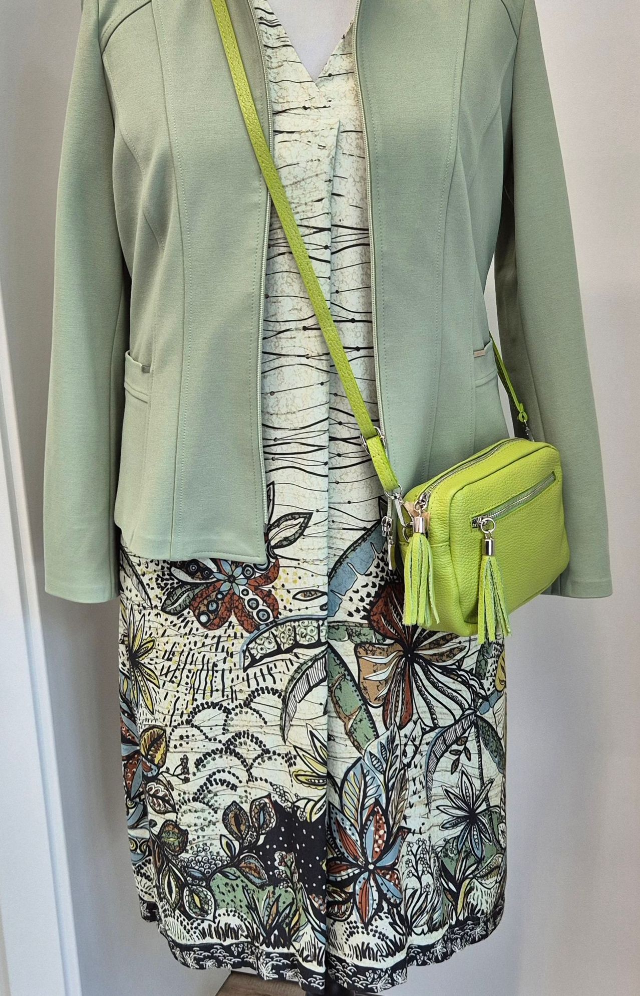 Ein Mannequin zeigt eine mintgrüne Jacke und einen passenden Blumenrock mit einer hellgrünen Umhängetasche.
