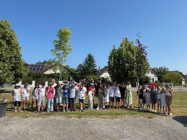 Eine Gruppe von Kindern und Erwachsenen posiert für ein Foto in einem Park mit Bäumen und Häusern im Hintergrund.