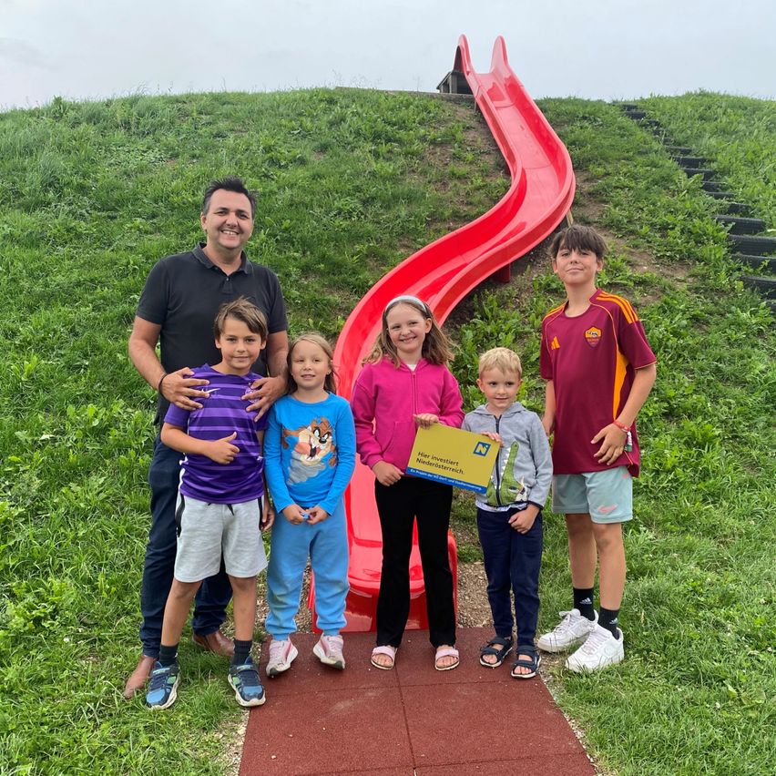 Eine Gruppe von Kindern und ein erwachsener Mann posieren für ein Foto vor einer roten Rutsche in einem Park.