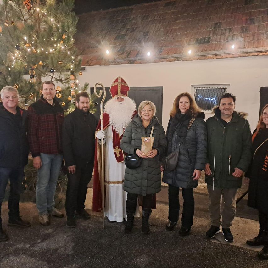 Eine Gruppe von Menschen in Winterkleidung posiert für ein Foto mit einem geschmückten Weihnachtsbaum und einem Mann als Weihnachtsmann vor einem Gebäude.
