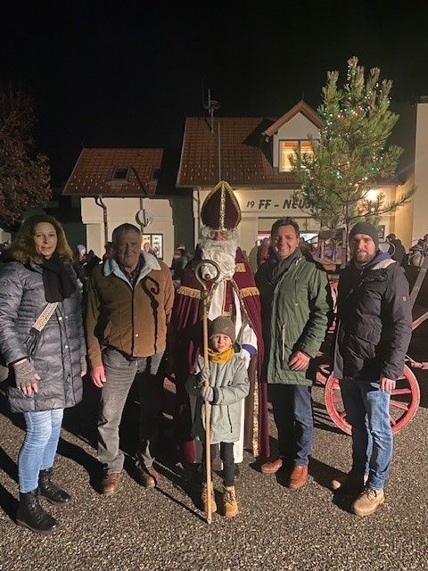 Fünf Personen stehen vor einem Gebäude. Ein als Weihnachtsmann verkleideter Mann steht in der Mitte und hält ein Kind. Sie alle lächeln für die Kamera.