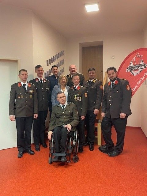 Eine Gruppe von Militärangehörigen und einer Frau in formeller Kleidung posiert für ein Foto in einem Raum mit rotem Bodenbelag.