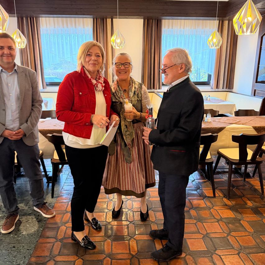 Vier Menschen stehen in einem Restaurant mit gefliesten Böden. Zwei Frauen und zwei Männer. Die Frauen halten ein Papier und ein Getränk. Die Männer tragen Brillen.