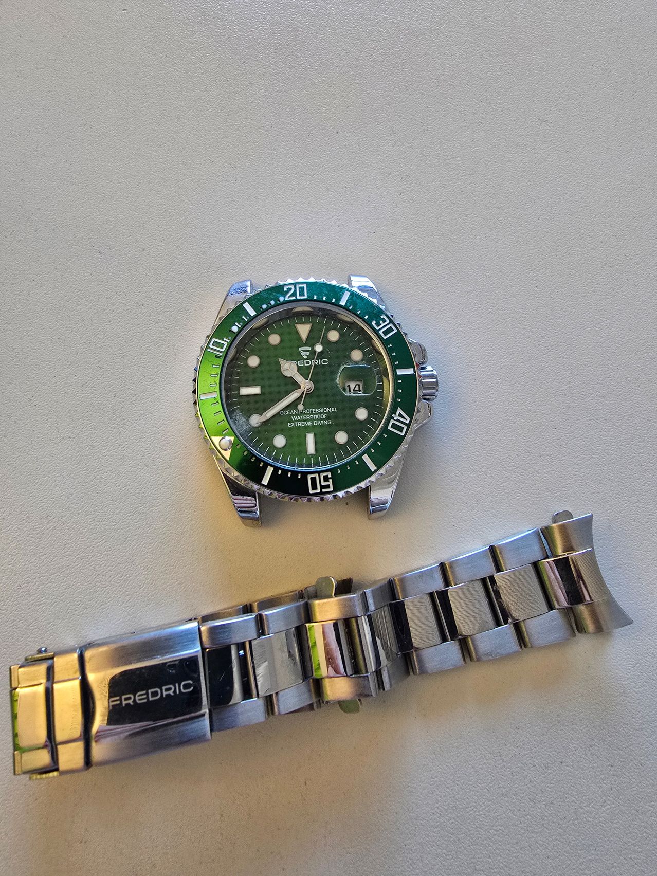 Eine Nahaufnahme einer grüngesichtigen Armbanduhr, mit der Aufschrift Ocean Professional, mit einem silbernen Armband, das den Namen Fredric trägt.