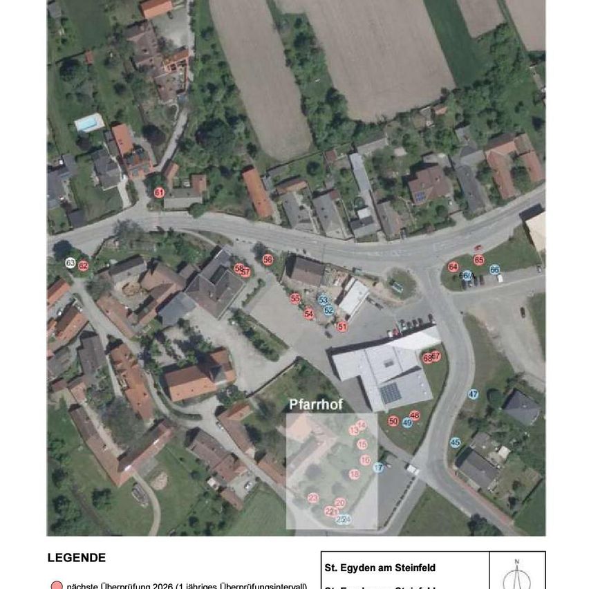 Eine Luftaufnahme zeigt ein ländliches Gebiet mit Häusern, einem Bauernhof und nummerierten Markierungen. Jedes Haus und Gebäude hat eine Nummer, und es gibt beschriftete Bereiche wie 'Pfarrhof'. Eine Legende am unteren Rand erklärt die Symbole.