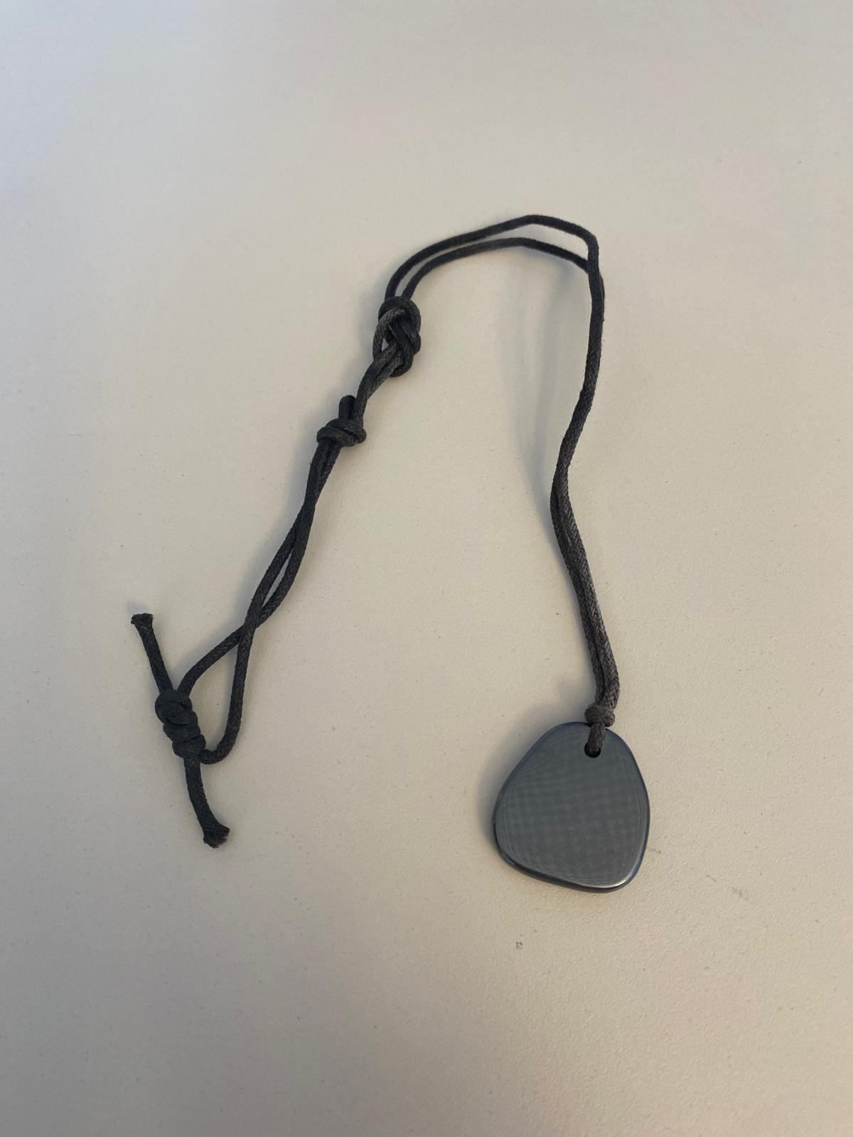 A black cord with a knotted end holds a silver-gray teardrop-shaped pendant. The pendant is smooth and metallic in appearance.