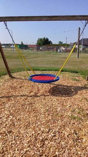 A colorful tire swing is suspended from a wooden frame on a playground covered with wood chips.