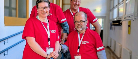 Fünf Menschen in roten T-Shirts und Ausweisen lächeln und stehen in einem Flur.