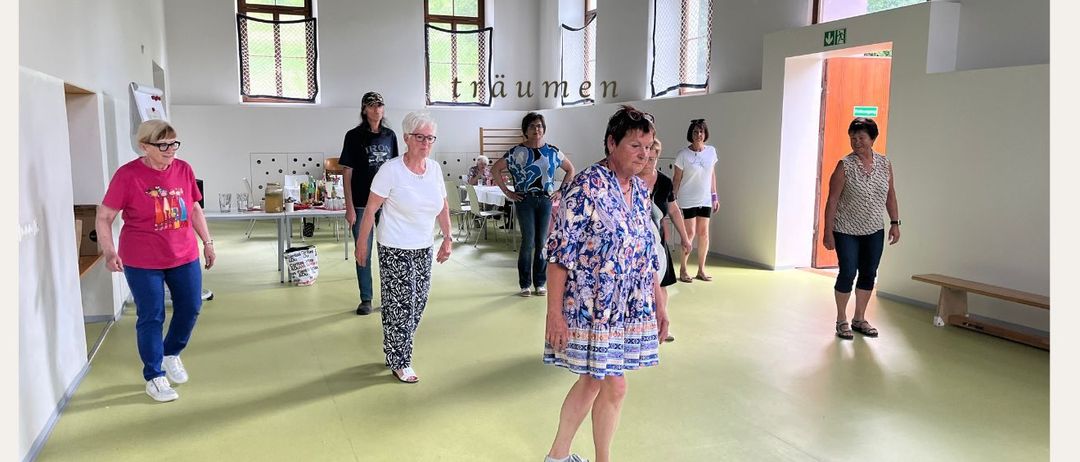 Vier Bilder einer Veranstaltung. Zwei Frauen tanzen gemeinsam. Eine Frau arbeitet an einem Laptop. Eine Gruppe von Menschen in einem Raum. Eine Person steht an einem Tisch.