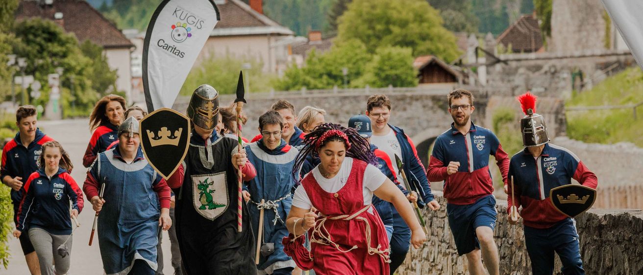 Eine Gruppe von Menschen in mittelalterlichen Kostümen läuft auf einem Pfad mit Bergen im Hintergrund.