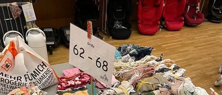 Ein Tisch ist mit einer Auswahl an Kinderkleidung gefüllt, ordentlich gefaltet und organisiert, mit einem Schild, das die Größen 62-68 anzeigt. Die Kleidung umfasst Kleider, Jeans, Hemden und Accessoires.
