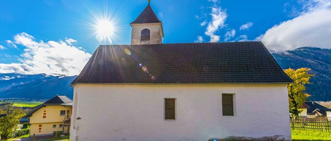 Eine weiße Kirche mit schwarzem Dach und einem Turm scheint unter der strahlenden Sonne mit blauem Himmel und Wolken.