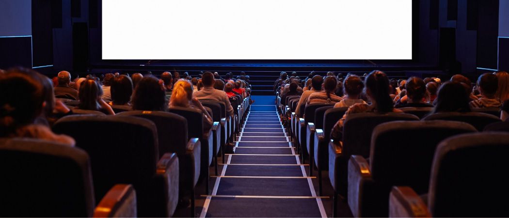 Ein Kinosaal mit vielen Menschen, die einen Film auf einer großen Leinwand sehen, mit Reihen von Stühlen und einem Teppichbodengang.