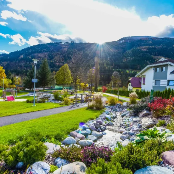 Ein sonniger Tag in einem Park mit einem Bach, Felsen und einem Berg im Hintergrund.