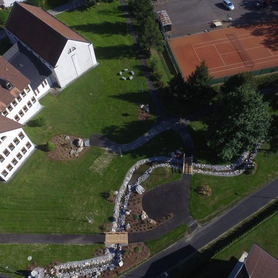 Eine Draufsicht auf ein großes Gebäude mit mehreren Fenstern. Ein Tennisplatz und ein Auto sind im Hintergrund zu sehen.