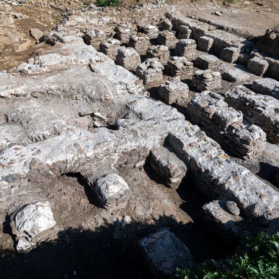 Eine archäologische Stätte mit großen, teilweise im Boden vergrabenen Steinstrukturen, mit verstreuten Steinen und Erde.