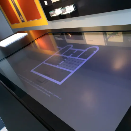 Ein digitales Display zeigt einen Grundriss mit Beschriftungen. Der Bereich scheint ein Ausstellungs- oder Informationsbereich zu sein.
