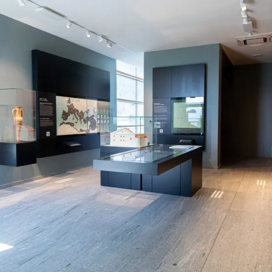 Das Innere eines Museums mit Holzboden. Vitrinen auf beiden Seiten einer zentralen Ausstellung mit einem Modell und Informationstafeln. Die Wände sind grau und die Decke hat eingelassene Beleuchtung.