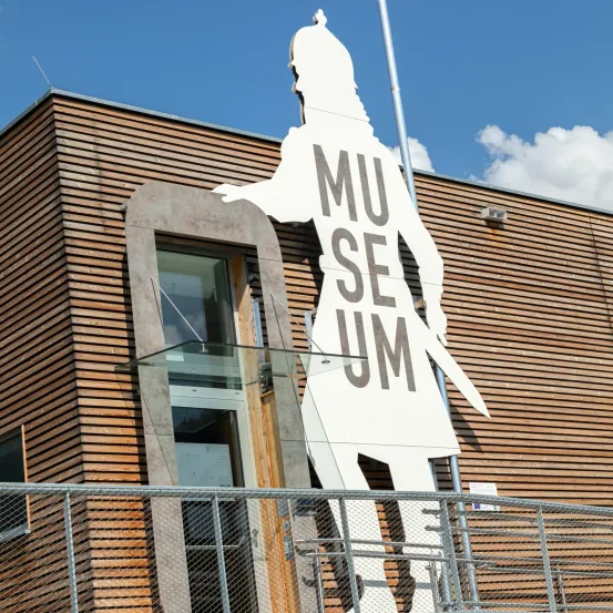 Ein Museumsgebäude mit einer großen weißen Aussparung einer Figur an der Seite, unter einem klaren blauen Himmel mit einigen Wolken.