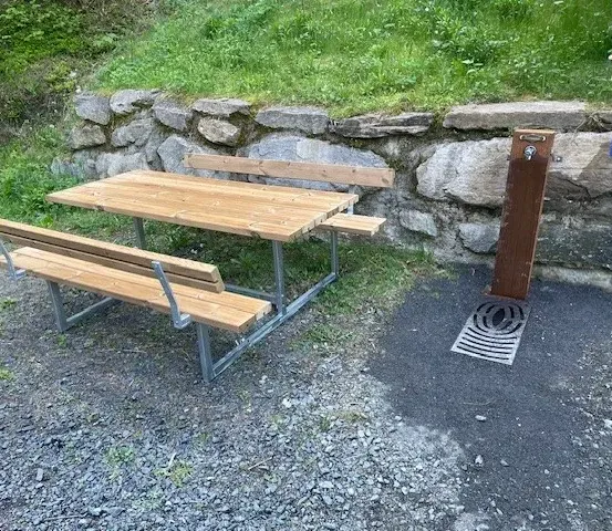 Eine Outdoor-Picknick-Tisch mit Bänken ist neben einer Steinmauer aufgestellt und verfügt über einen Wasserbrunnen.