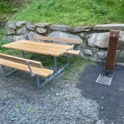 Eine Outdoor-Picknick-Tisch mit Bänken ist neben einer Steinmauer aufgestellt und verfügt über einen Wasserbrunnen.