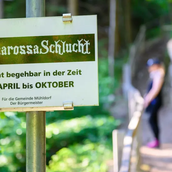Ein Schild an einem Pfosten weist darauf hin, dass der Barbarossa Schluch von April bis Oktober begehbar ist. Das Schild ist für die Gemeinde Mühldorf vom Bürgermeister.