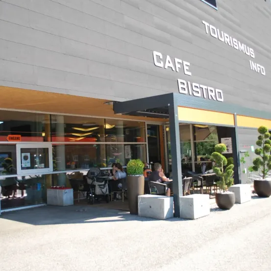 Der Eingang eines Cafes und Bistros namens Tourismus Info, mit einigen Leuten, die draußen unter einem Vordach sitzen.