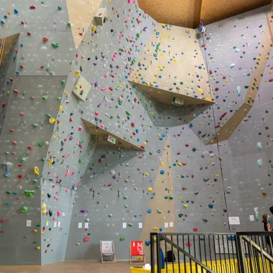 Eine Indoor-Kletterwand mit verschiedenfarbigen Griffen und einer Person in der Nähe der Treppe.
