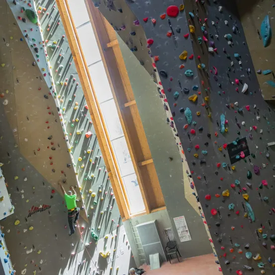 Ein Mann klettert an einer Kletterwand mit einem hellen Licht im Hintergrund. Bunte Steine schmücken die Wand.