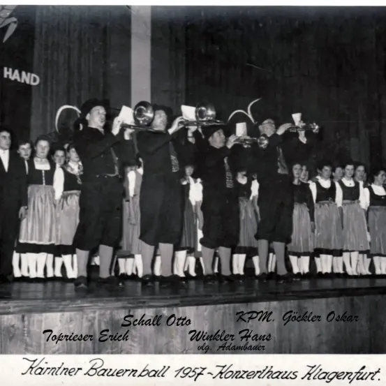 Ein Schwarz-Weiß-Foto einer Gruppe von Menschen auf der Bühne. Sie halten Musikinstrumente. Der Text lautet: Toprieser Erich, Schall Otto, Winkler Hans, RKM Gockler Oskar und Adambauer. Am unteren Rand des Bildes steht: Karntner Bauernball 1957-Honzethaus Klagenfurt.
