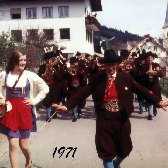 Eine Frau und ein Mann in traditioneller Kleidung gehen 1971 in einer Parade mit einer Marschkapelle.