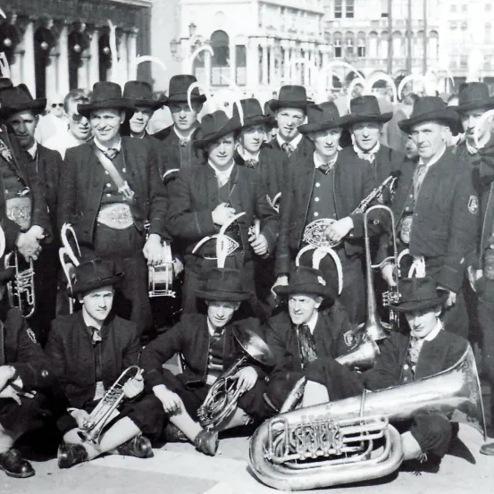 Ein Schwarz-Weiß-Bild einer Brassband, alle in passenden Uniformen und Hüten gekleidet, posieren für ein Gruppenfoto. Die Instrumente umfassen Trompeten, Posaunen und Tubas.