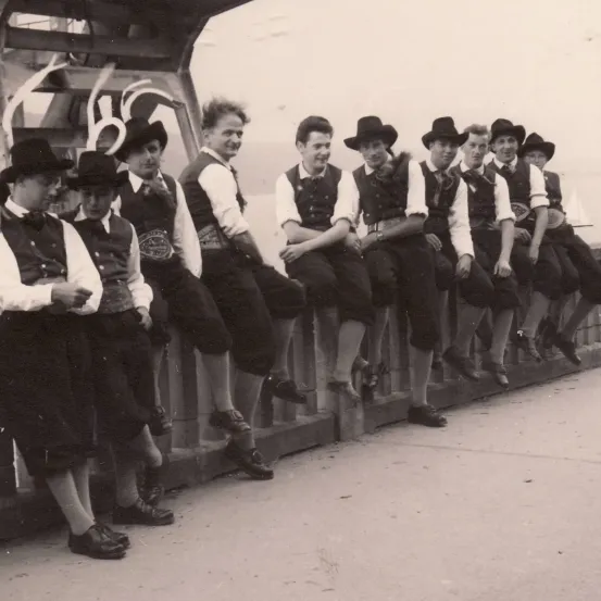 Ein Schwarz-Weiß-Foto einer Gruppe junger Männer in traditioneller Kleidung, die auf einer Brückenbrüstung sitzen.
