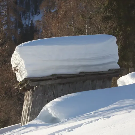 Eine hölzerne Struktur, die von dickem Schnee bedeckt ist, umgeben von schneebedeckten Bäumen in einem Gebirgsgebiet.