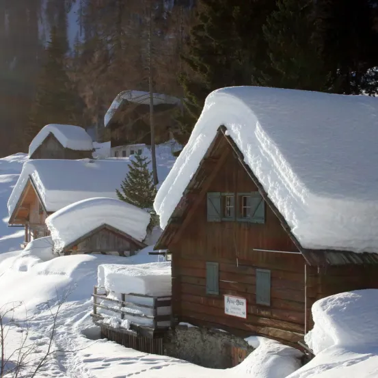 Ein schneebedecktes Holzhaus mit einem Schild, umgeben von schneebedeckten Häusern und Bäumen.